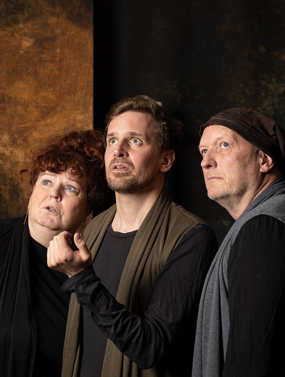 Billede fra forestillingen- En kvinde og to mænd, som står skulder ved skulder og kigger op 